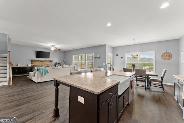 kitchen with dark brown cabinetry, dark wood finished floors, light stone counters, a kitchen breakfast bar, and ceiling fan with notable chandelier