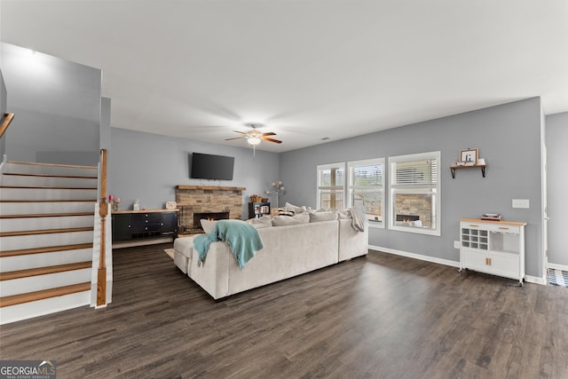 living area featuring a fireplace, a ceiling fan, baseboards, stairs, and dark wood-style floors