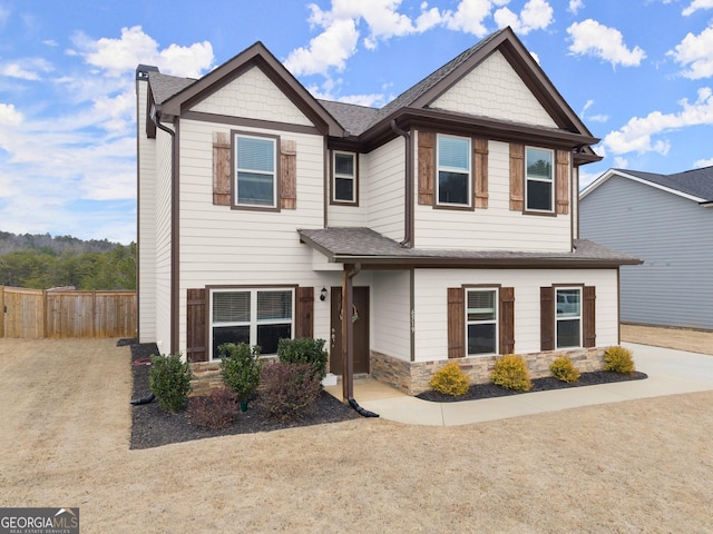 craftsman-style home with stone siding, roof with shingles, and fence