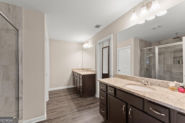 bathroom featuring wood finished floors, two vanities, a sink, visible vents, and a shower stall