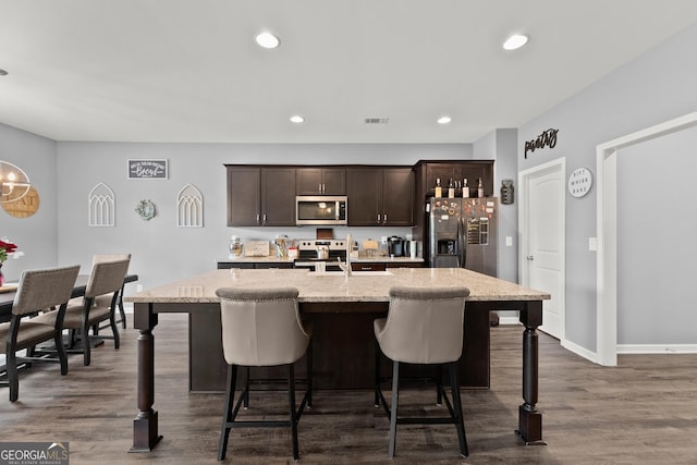 kitchen with dark wood-type flooring, visible vents, a kitchen breakfast bar, dark brown cabinets, and appliances with stainless steel finishes