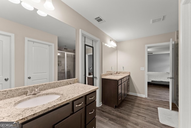 ensuite bathroom with a stall shower, visible vents, a sink, and wood finished floors