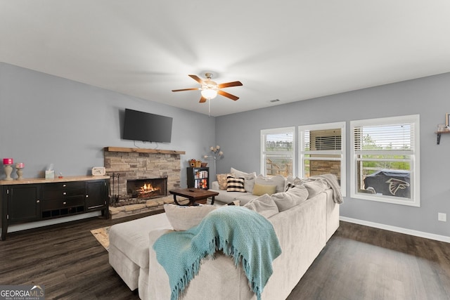 living area featuring visible vents, dark wood-type flooring, ceiling fan, a stone fireplace, and baseboards