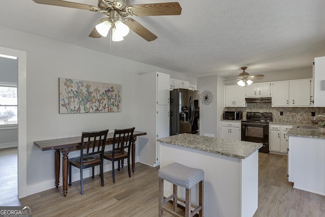 kitchen with light wood-style flooring, under cabinet range hood, a sink, backsplash, and black appliances