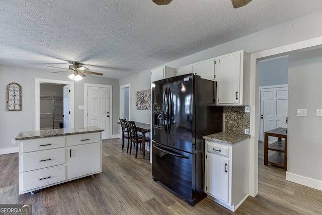 kitchen featuring dark wood-type flooring, a ceiling fan, white cabinets, black fridge, and tasteful backsplash