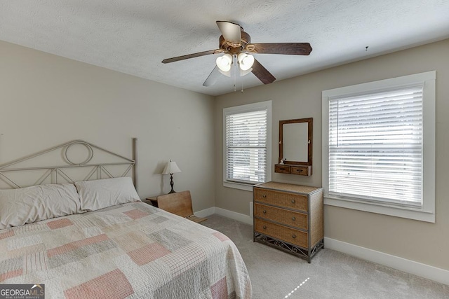 bedroom featuring baseboards, a textured ceiling, a ceiling fan, and light colored carpet