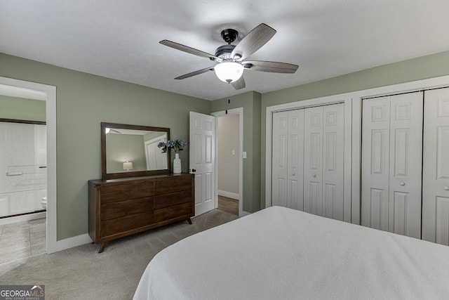 carpeted bedroom with ensuite bath, baseboards, ceiling fan, and two closets