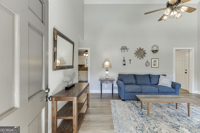 living room featuring a high ceiling, light wood-style floors, ornamental molding, a ceiling fan, and baseboards