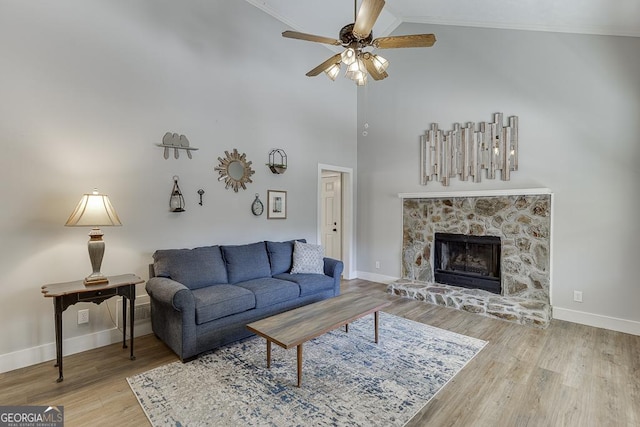 living area featuring ceiling fan, a stone fireplace, baseboards, and wood finished floors