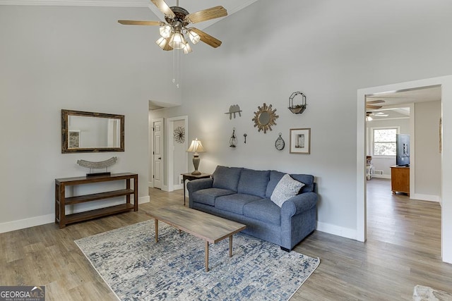 living area featuring a ceiling fan, a high ceiling, baseboards, and light wood finished floors