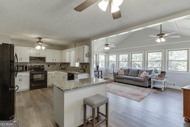 kitchen featuring light stone counters, wood finished floors, under cabinet range hood, black appliances, and white cabinetry