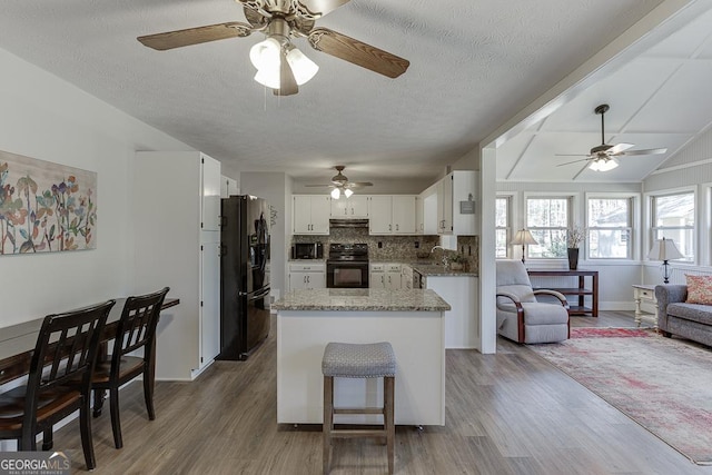 kitchen featuring white cabinets, open floor plan, wood finished floors, under cabinet range hood, and black appliances