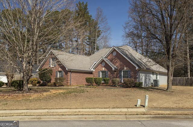 view of front of house with cooling unit, brick siding, fence, and roof with shingles