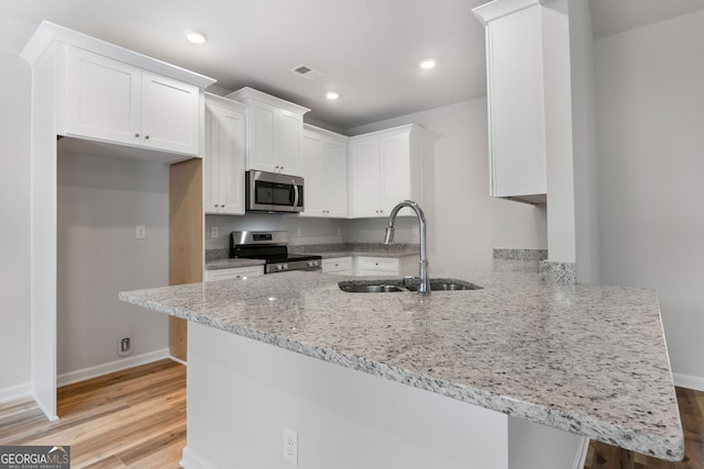 kitchen with light stone counters, a peninsula, visible vents, white cabinetry, and appliances with stainless steel finishes