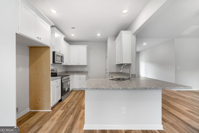 kitchen featuring light wood finished floors, recessed lighting, appliances with stainless steel finishes, a sink, and a peninsula