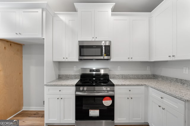 kitchen featuring light wood finished floors, baseboards, white cabinets, appliances with stainless steel finishes, and light stone counters