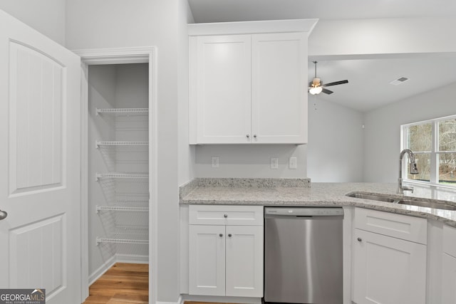 kitchen featuring white cabinets, light stone counters, light wood-type flooring, stainless steel dishwasher, and a sink