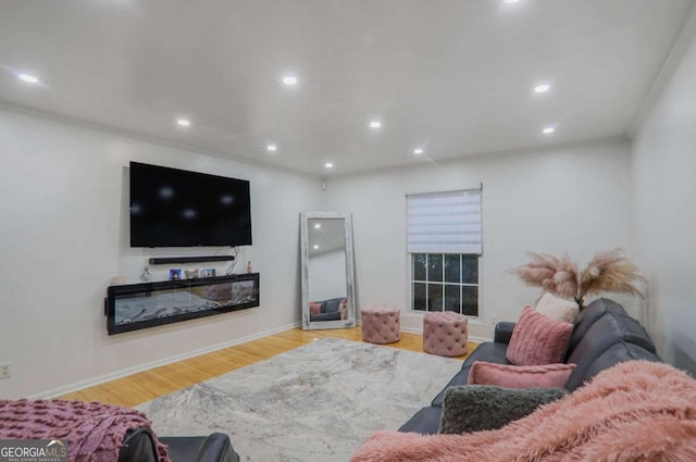 living area featuring baseboards, a glass covered fireplace, ornamental molding, wood finished floors, and recessed lighting