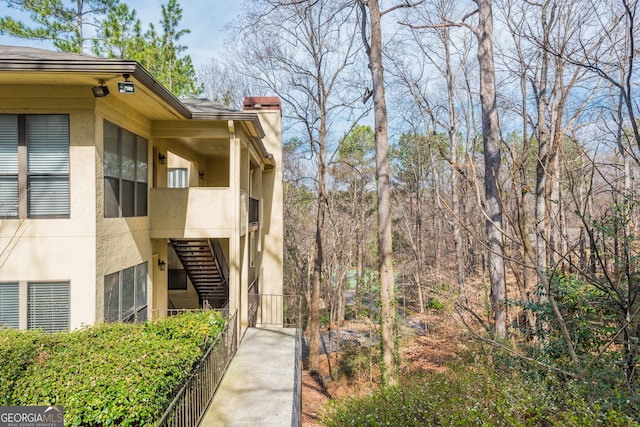 view of side of property featuring fence, stairway, and stucco siding