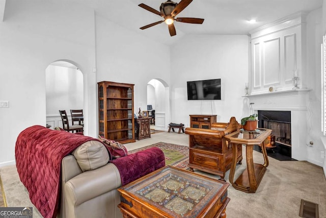 living room featuring arched walkways, light colored carpet, a large fireplace, a ceiling fan, and vaulted ceiling