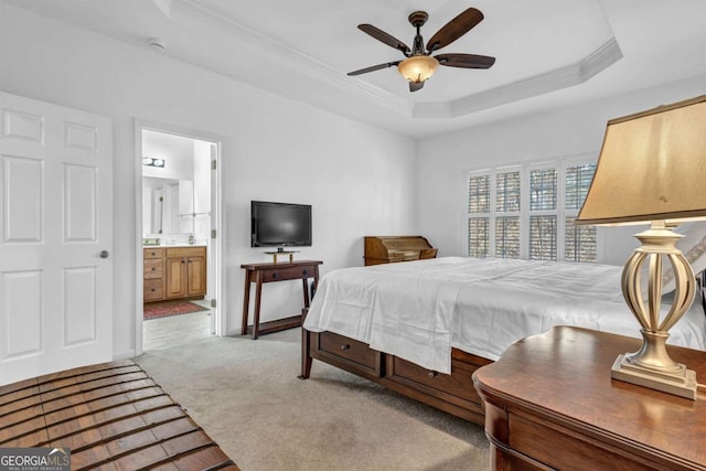 bedroom featuring light carpet, baseboards, a raised ceiling, ensuite bath, and crown molding