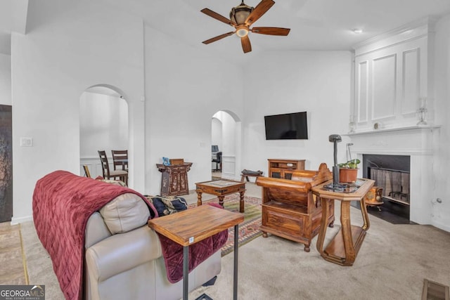 living room with arched walkways, ceiling fan, a high ceiling, a fireplace with flush hearth, and visible vents