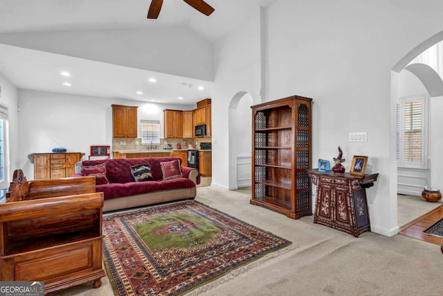 living room with arched walkways, high vaulted ceiling, and light colored carpet