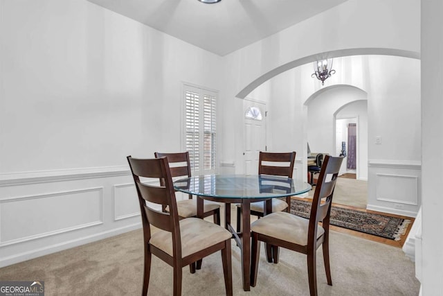 dining space featuring arched walkways, a decorative wall, an inviting chandelier, and light colored carpet