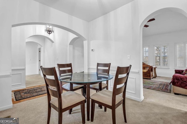 dining area featuring arched walkways, a decorative wall, light carpet, wainscoting, and an inviting chandelier