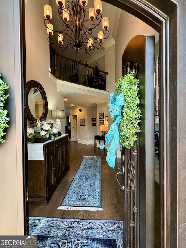 foyer entrance with crown molding, a towering ceiling, an inviting chandelier, and wood finished floors