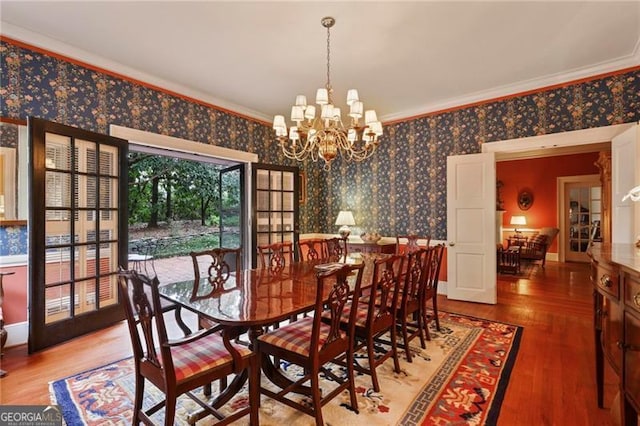 dining space featuring wood finished floors, a chandelier, crown molding, and wallpapered walls