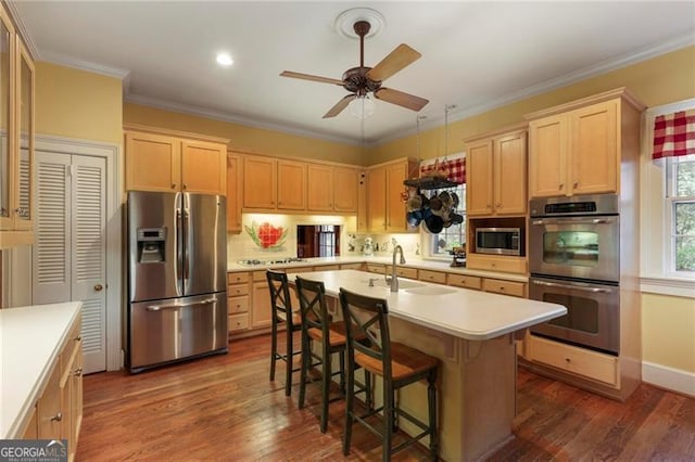 kitchen featuring a kitchen island with sink, ornamental molding, a sink, light countertops, and appliances with stainless steel finishes