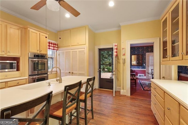 kitchen with a breakfast bar area, ornamental molding, appliances with stainless steel finishes, wood finished floors, and a sink