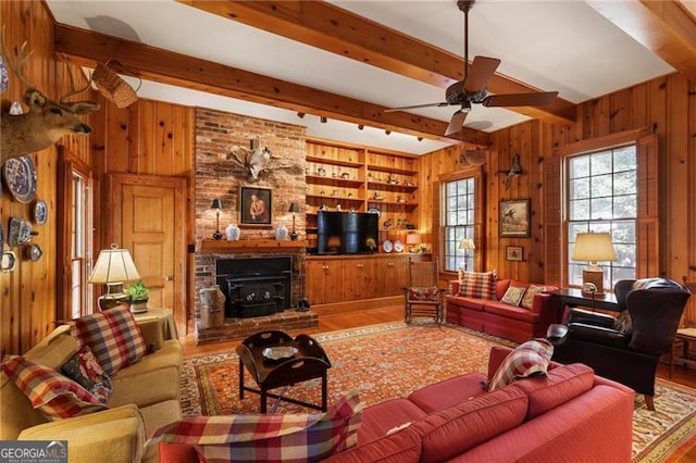 living area with beam ceiling, wooden walls, a ceiling fan, and wood finished floors