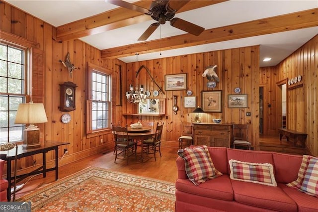 living room with beam ceiling, wood finished floors, a ceiling fan, and wood walls