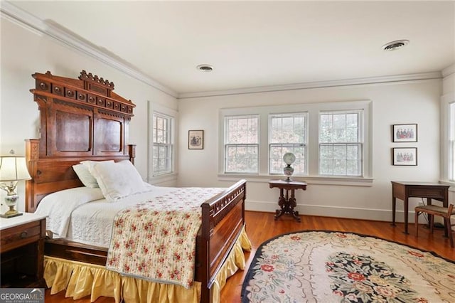 bedroom featuring visible vents, wood finished floors, baseboards, and ornamental molding