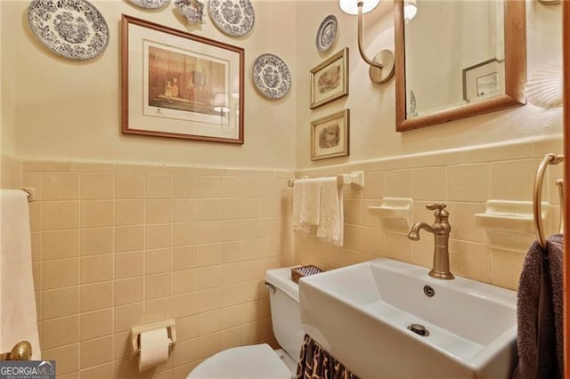 bathroom featuring tile walls, toilet, a wainscoted wall, and a sink