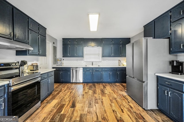 kitchen with dark wood-type flooring, stainless steel appliances, light countertops, under cabinet range hood, and a sink