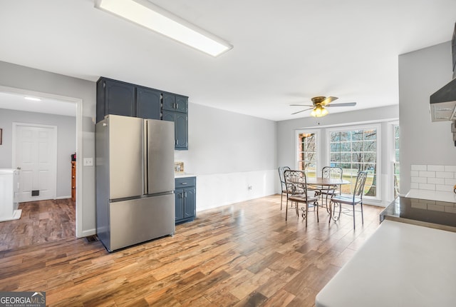 kitchen featuring light countertops, a ceiling fan, freestanding refrigerator, blue cabinets, and light wood-type flooring