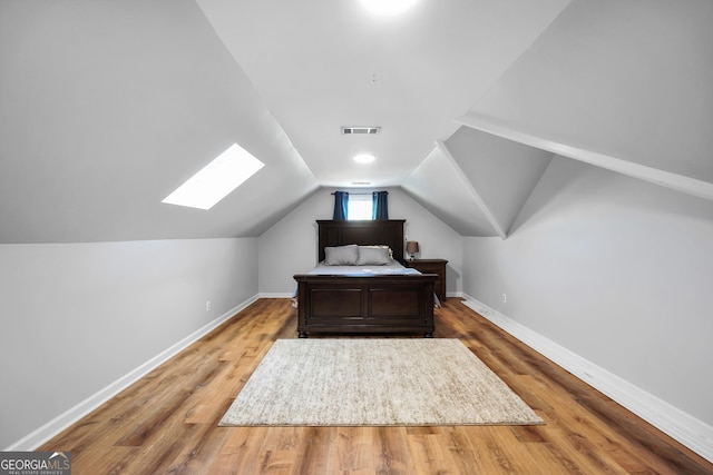 bedroom featuring vaulted ceiling with skylight, baseboards, visible vents, and wood finished floors