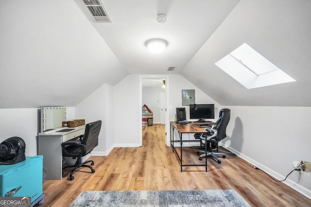 office space featuring baseboards, vaulted ceiling with skylight, visible vents, and light wood-style floors