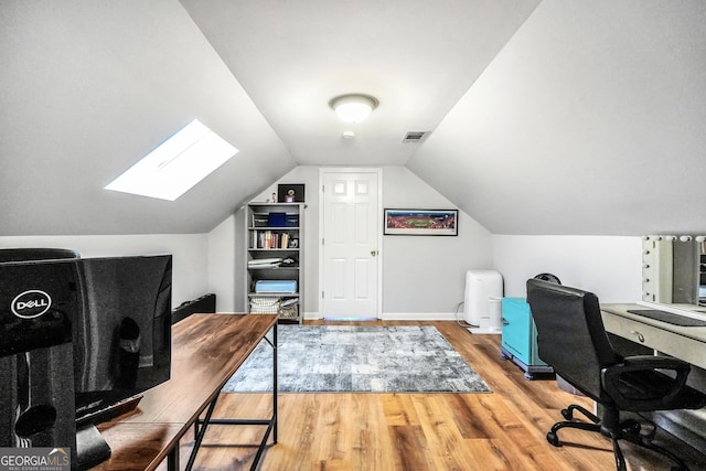 home office with lofted ceiling with skylight, baseboards, visible vents, and wood finished floors