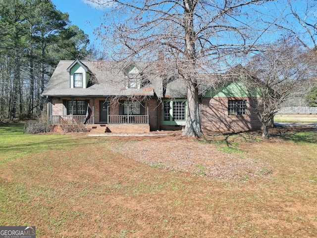 cape cod-style house featuring covered porch, a front lawn, roof with shingles, and brick siding