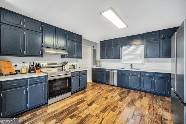 kitchen featuring appliances with stainless steel finishes, dark wood-style flooring, light countertops, under cabinet range hood, and a sink