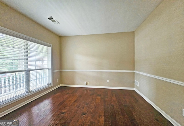 empty room featuring dark wood-style flooring, visible vents, and baseboards