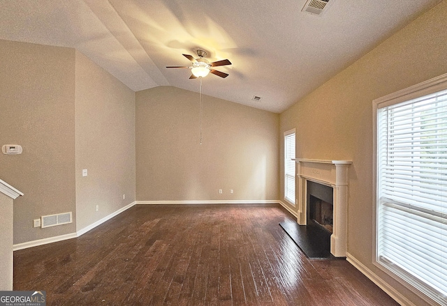 unfurnished living room featuring dark wood finished floors, lofted ceiling, visible vents, a fireplace with raised hearth, and a ceiling fan