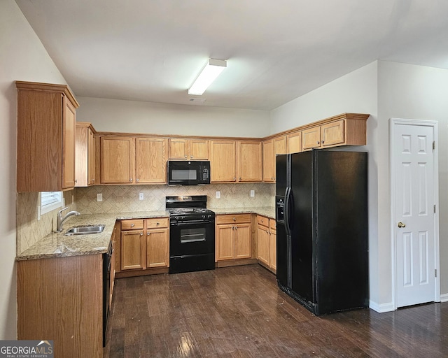 kitchen with dark wood-type flooring, a sink, light stone countertops, black appliances, and backsplash