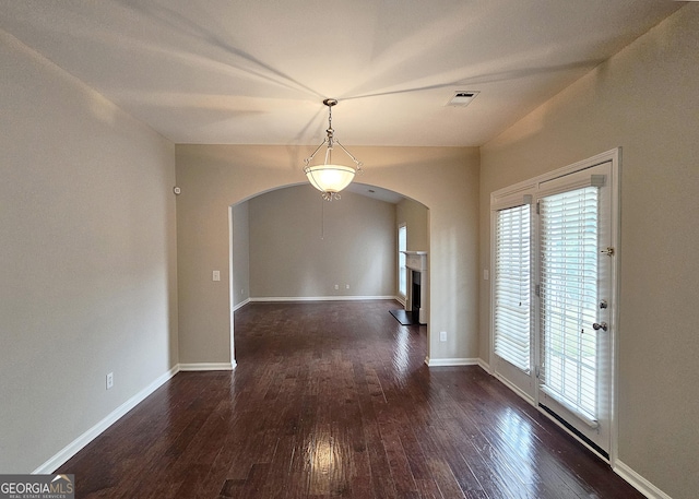 unfurnished dining area with arched walkways, visible vents, a fireplace with raised hearth, wood finished floors, and baseboards