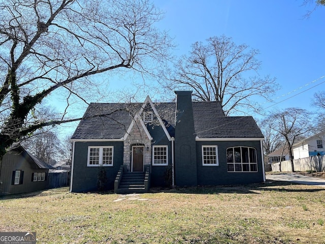 view of front facade with a shingled roof, fence, a chimney, and a front lawn