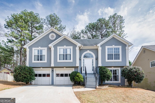 raised ranch with a garage, driveway, fence, and stucco siding